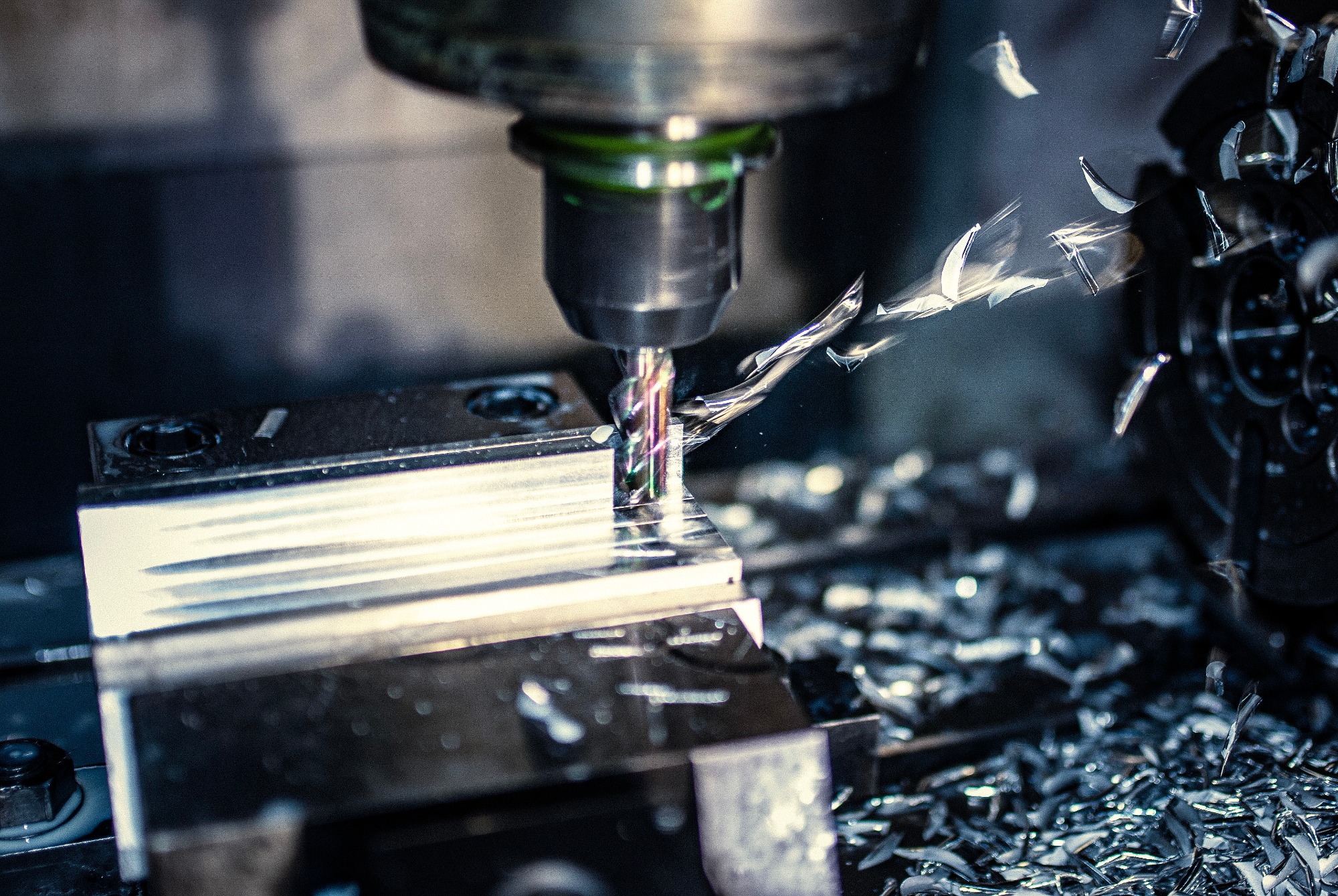 Frezarka CNC w trakcie obróbki metalowego elementu; wióry rozsypane wokół, chłodziwo rozpryskuje się spod freza.