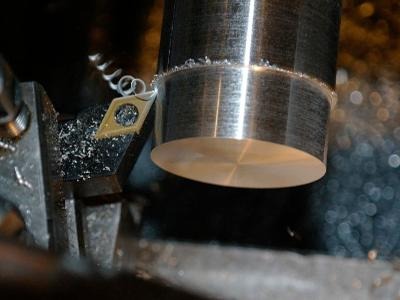 Detail metalowego przedmiotu w trakcie obróbki skrawaniem na tokarce, wióry i chłodziwo wokół ostrza