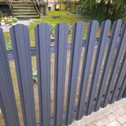 Grafitowe ogrodzenie panelowe z metalowymi słupkami, widoczne na tle zielonego trawnika i schodów wejściowych do domu w Kamieńcu.