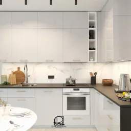 Nowoczesna, biała kuchnia z czarnym blatem, marmurowym backsplash'em i złotymi uchwytami, oświetlona punktowymi lampami sufitowymi, z okrągłym stołem jadalnym i dekoracyjnymi elementami.