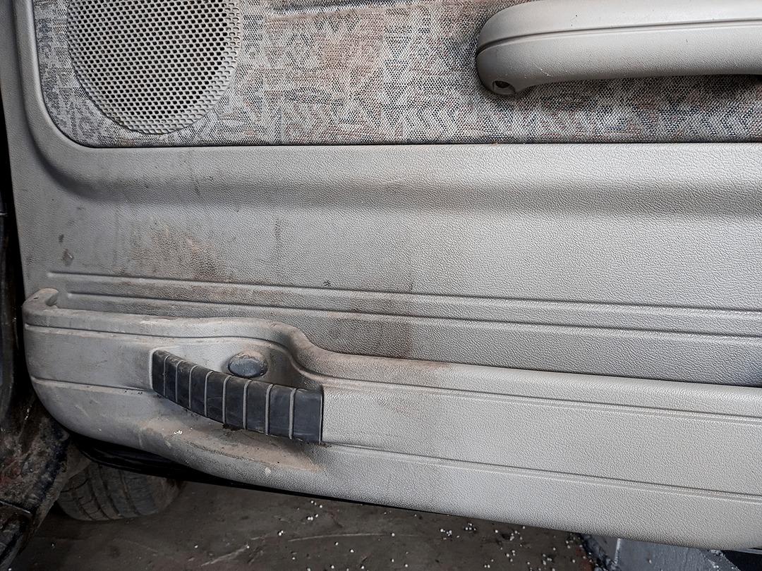 Brudny panel drzwi samochodu z widocznymi śladami użytkowania i zabrudzeniami na tapicerce i plastiku.