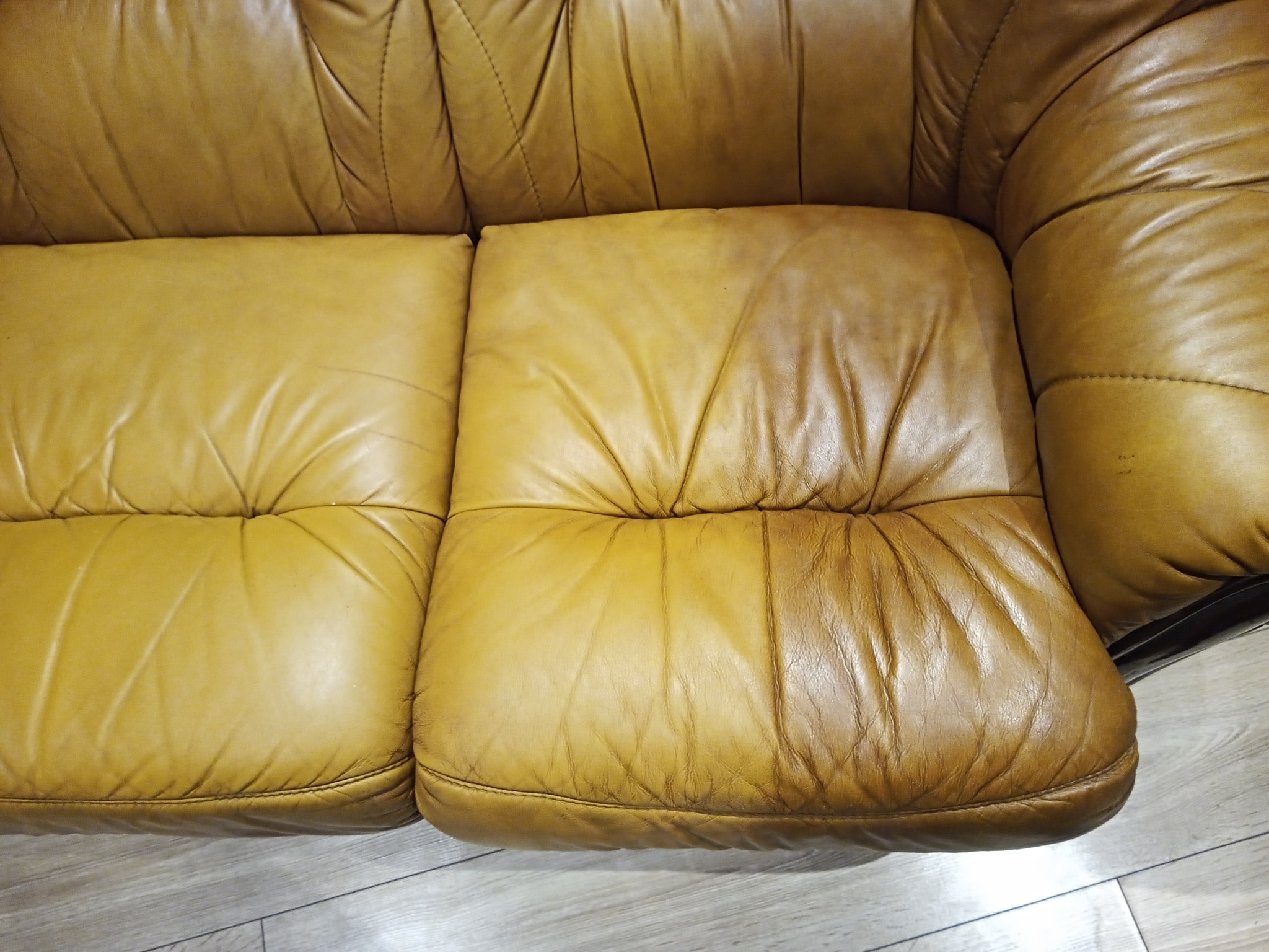 Fragment sofy z żółtej skóry z widocznymi śladami użytkowania, w tym plamy i zarysowania, ukazujący potrzebę czyszczenia i renowacji tapicerki.