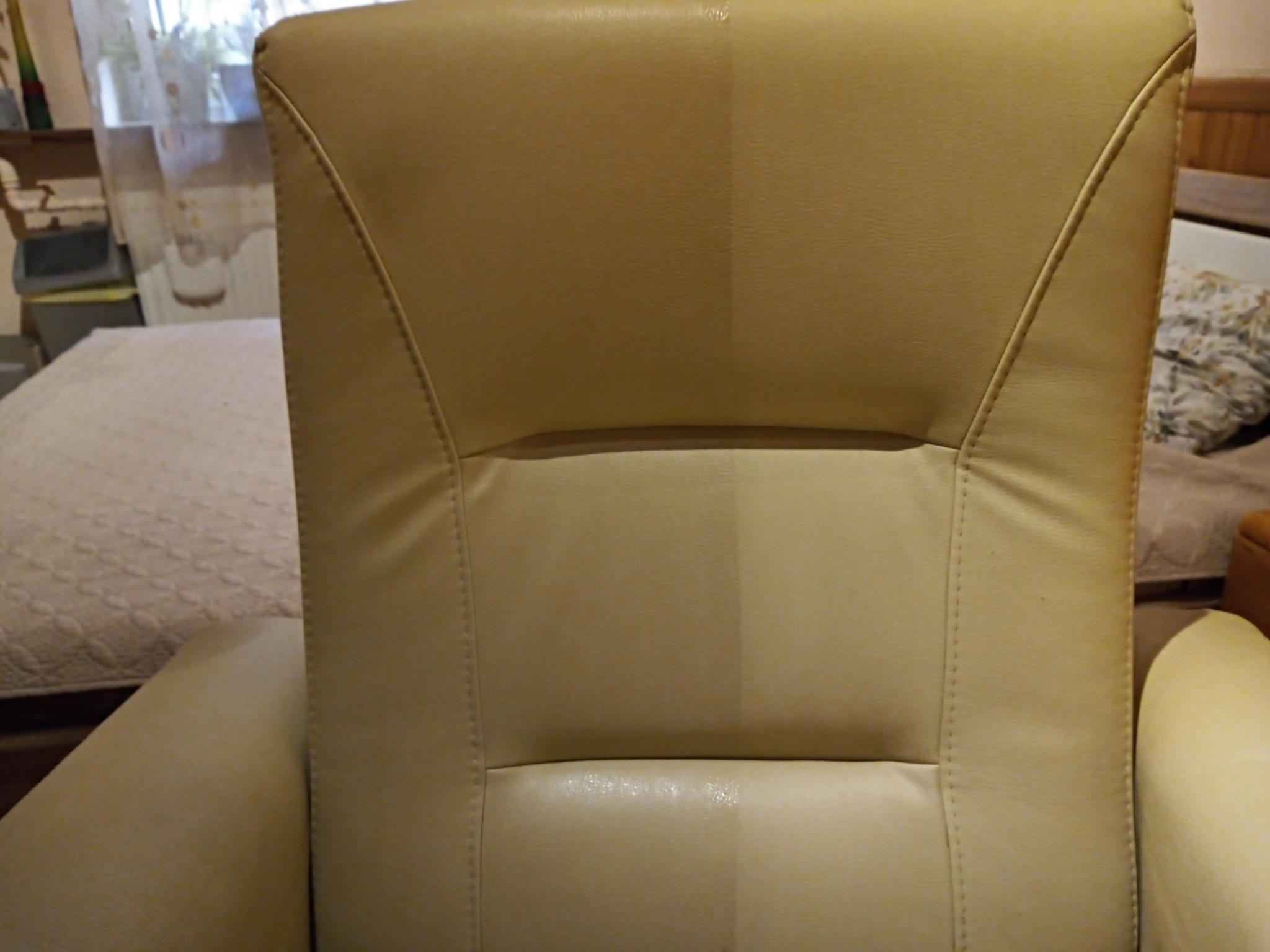 Beżowy fotel z widoczną różnicą w czystości tapicerki po jednej stronie, na tle sypialni.