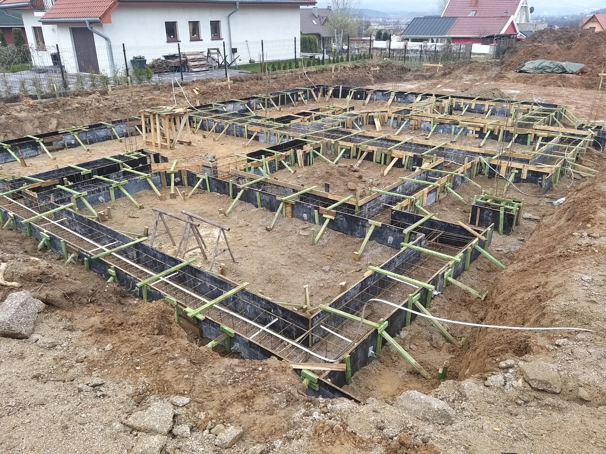 Przygotowanie fundamentów pod budowę domu: szalunki zbrojeniowe, drewniane podpory i wykopane rowy w ziemi.