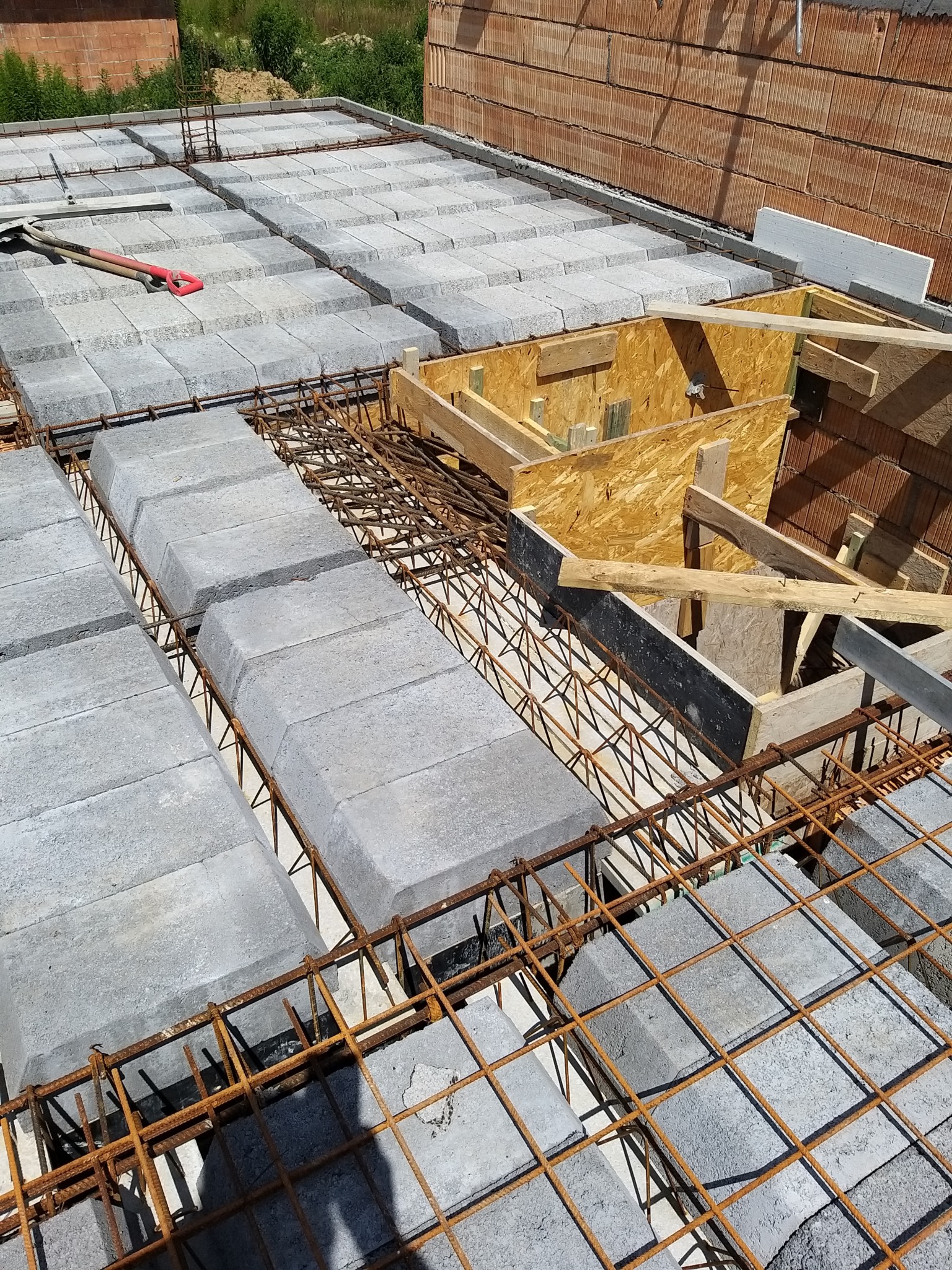 Budowa stropu Teriva: betonowe pustaki ułożone na stalowym zbrojeniu, widoczne drewniane szalunki i fragment muru z cegły ceramicznej w tle.