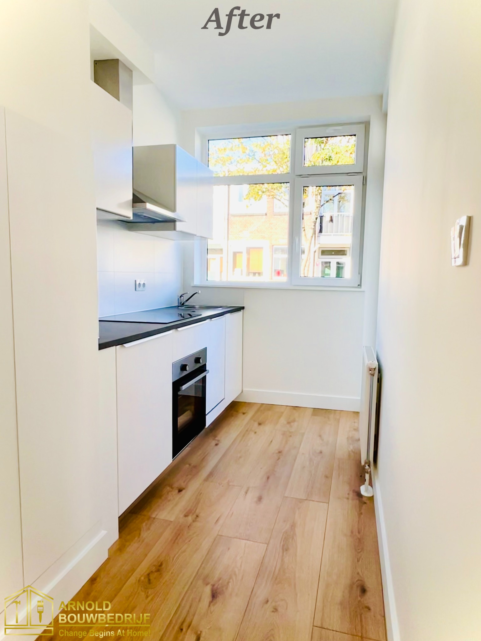 Jasna, mała kuchnia po remoncie z białymi szafkami, czarnym blatem, drewnianą podłogą i oknem z widokiem na budynek z czerwonej cegły.