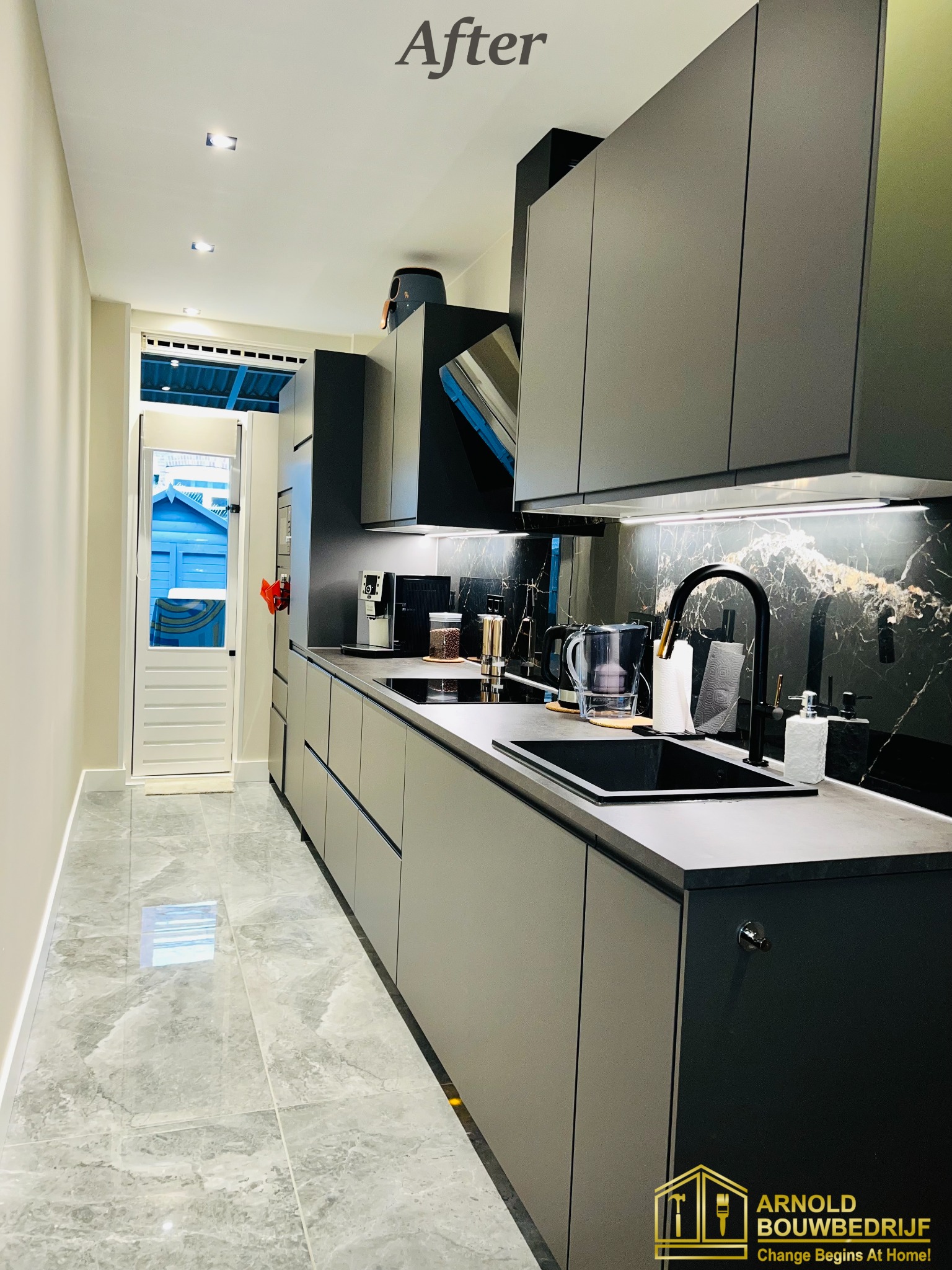 Nowoczesna kuchnia po remoncie, szare szafki z czarnym blatem i marmurowym backsplash, widok na drzwi wejściowe i ogród, podłoga z szarego marmuru.