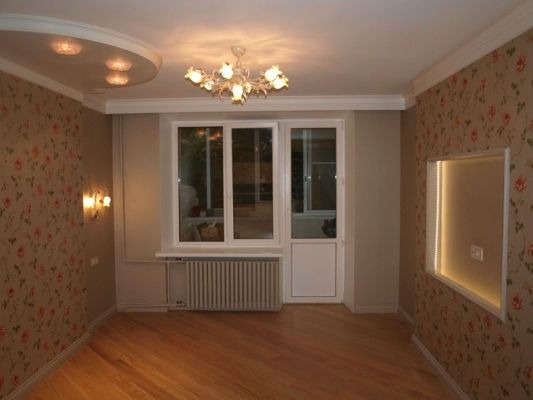 Wykończone wnętrze pokoju z drewnianą podłogą, ścianami w kwiatowe tapety, oknem z balkonem, dekoracyjnym oświetleniem sufitowym i wnęką z podświetleniem LED.