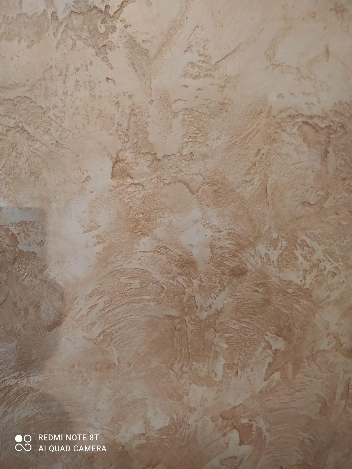 Beżowa ściana z dekoracyjną fakturą imitującą kamień, wykonana techniką szpachlowania strukturalnego.