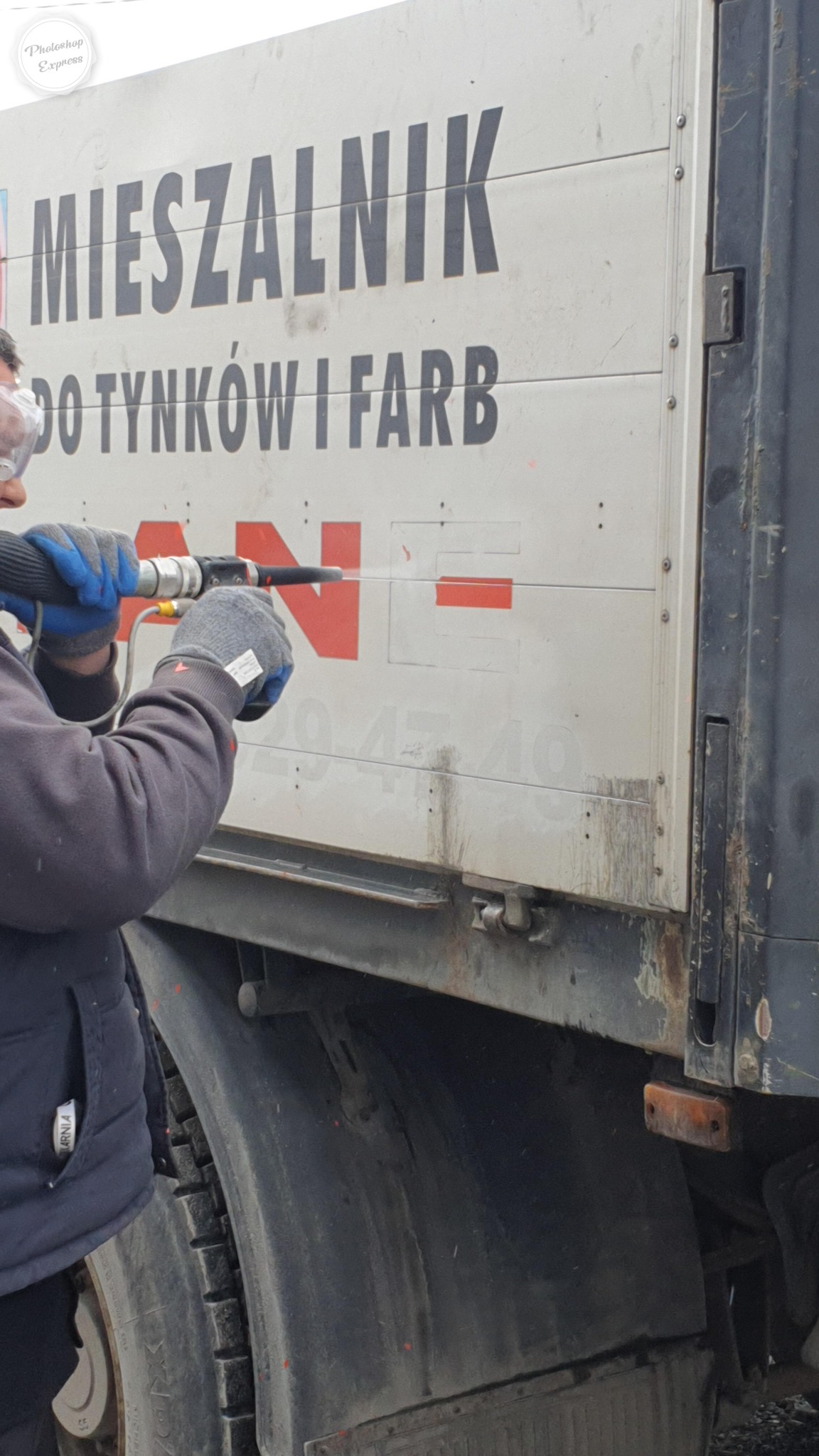 Pracownik w okularach ochronnych czyści zewnętrzną ścianę brudnej furgonetki z napisem 'MIESZALNIK DO TYNKÓW I FARB' za pomocą urządzenia do czyszczenia pod ciśnieniem, widoczne ślady brudu i rdzy.