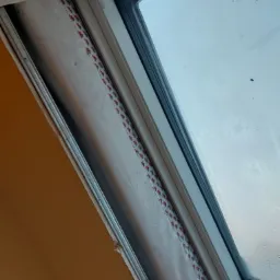 Okno dachowe z widoczną warstwą szpachli zabezpieczoną taśmą malarską przed malowaniem ściany, widoczne niedoskonałości na ścianie.