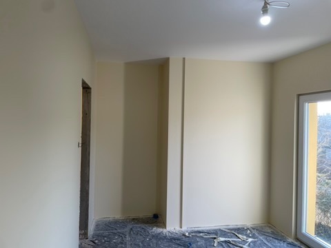 Pomalowane na kremowo wnętrze z widocznym zabezpieczeniem podłogi folią malarską i surową ościeżnicą drzwiową.