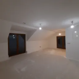 Poddasze po wykonaniu gładzi, widoczne ślady szlifowania na podłodze, przygotowane do dalszych prac wykończeniowych, z dwoma parami drewnianych drzwi.