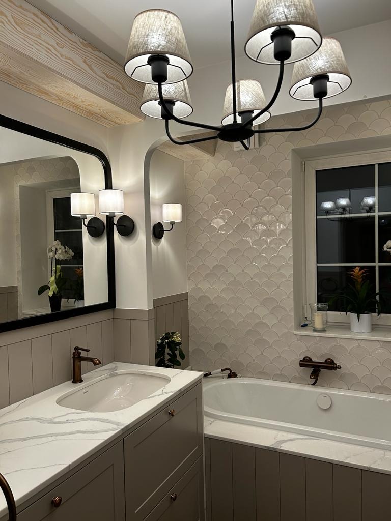 Wykończona łazienka w stylu klasycznym z wanną, umywalką nablatową z marmurowym blatem, lustrem w czarnej ramie, oświetleniem ściennym i wiszącym żyrandolem.