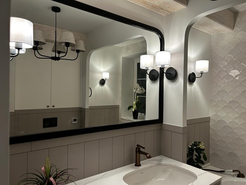 Nowoczesna łazienka z dużym lustrem w czarnej ramie, marmurowym blatem, białą umywalką i armaturą w kolorze miedzi. Na ścianie ozdobne płytki w kształcie rybiej łuski oraz czarne kinkiety z białymi...