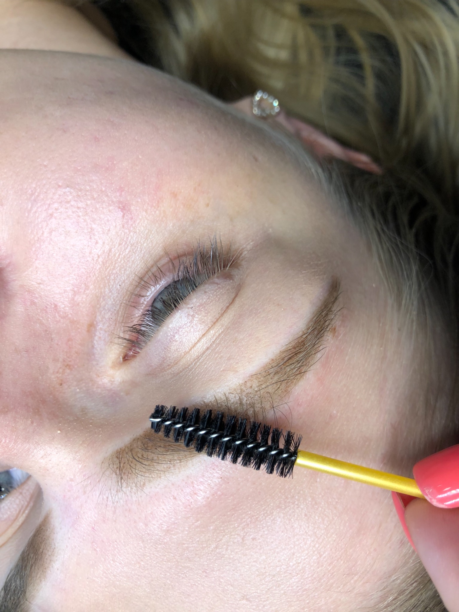 Kobieta z bliska podczas stylizacji brwi, użycie szczoteczki z żółtą rączką do układania włosków.