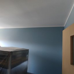 PAUL & ZBIG USŁUGI REMONTOWO - BUDOWLANE PAWEŁ FIJAŁKOWSKI & ZBIGNIEW ZALEWSKI S.C. - Pokój z pomalowanymi na niebiesko ścianami, biały sufit z wystającymi kablami, meble zabezpieczone folią ochronną, widoczny fragment futryny drzwi.