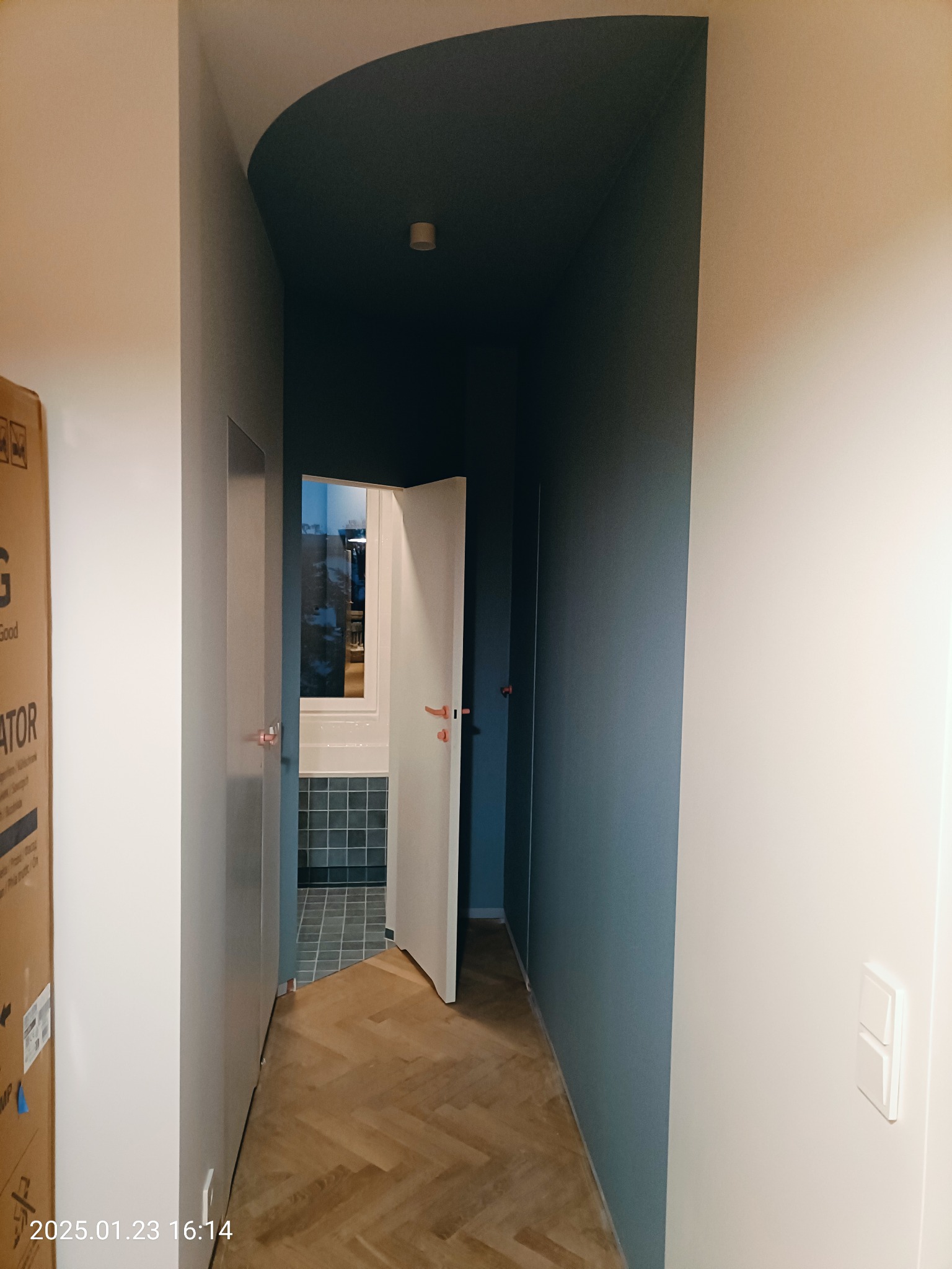 Korytarz po remoncie z parkietem w jodełkę, pomalowanym sufitem na ciemny kolor i otwartymi drzwiami do łazienki z szarą glazurą.