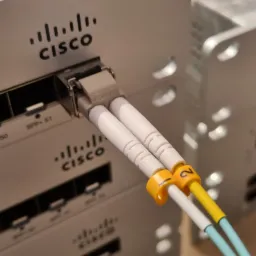 Fragment szafy serwerowej z przełącznikami Cisco, do portu SFP+ 51 podłączone dwa kable światłowodowe oznaczone numerami 1 i 2 na żółtych opaskach.