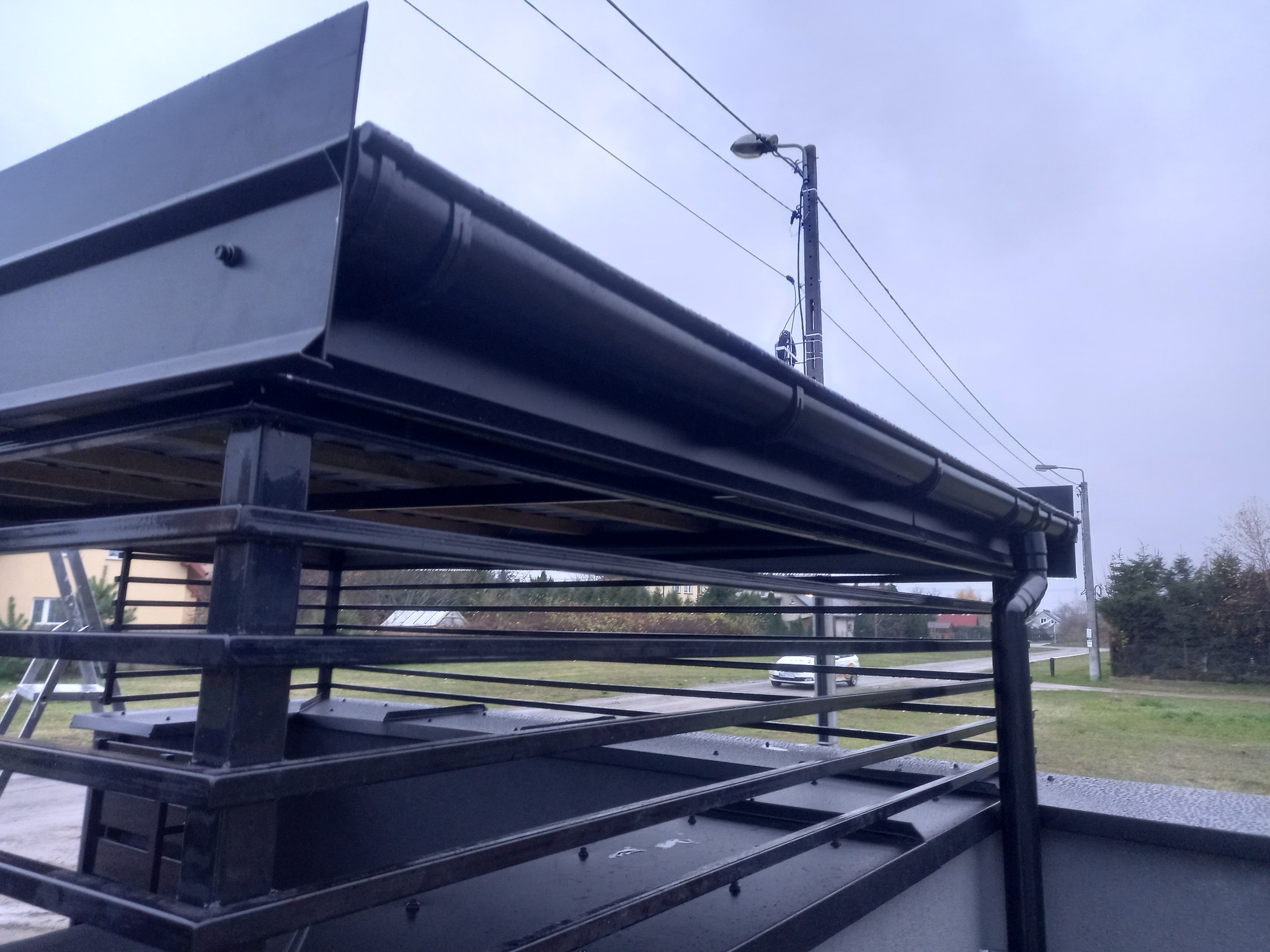 Konstrukcja dachu z zamontowaną, ciemną rynną, widok na ulicę i latarnię