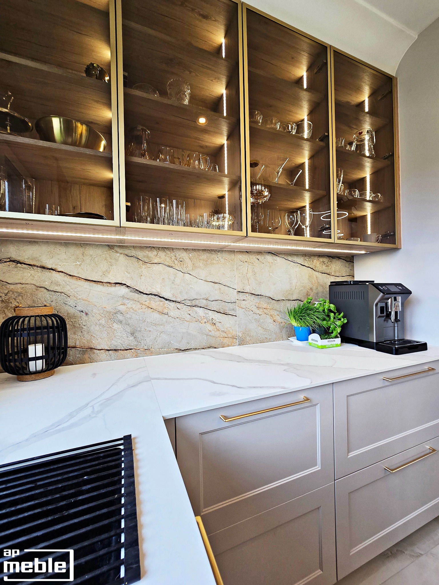 Elegancka kuchnia: szare szafki z złotymi uchwytami, marmurowy blat, przeszklone szafki wiszące z oświetleniem LED i dekoracyjnymi naczyniami w tle.