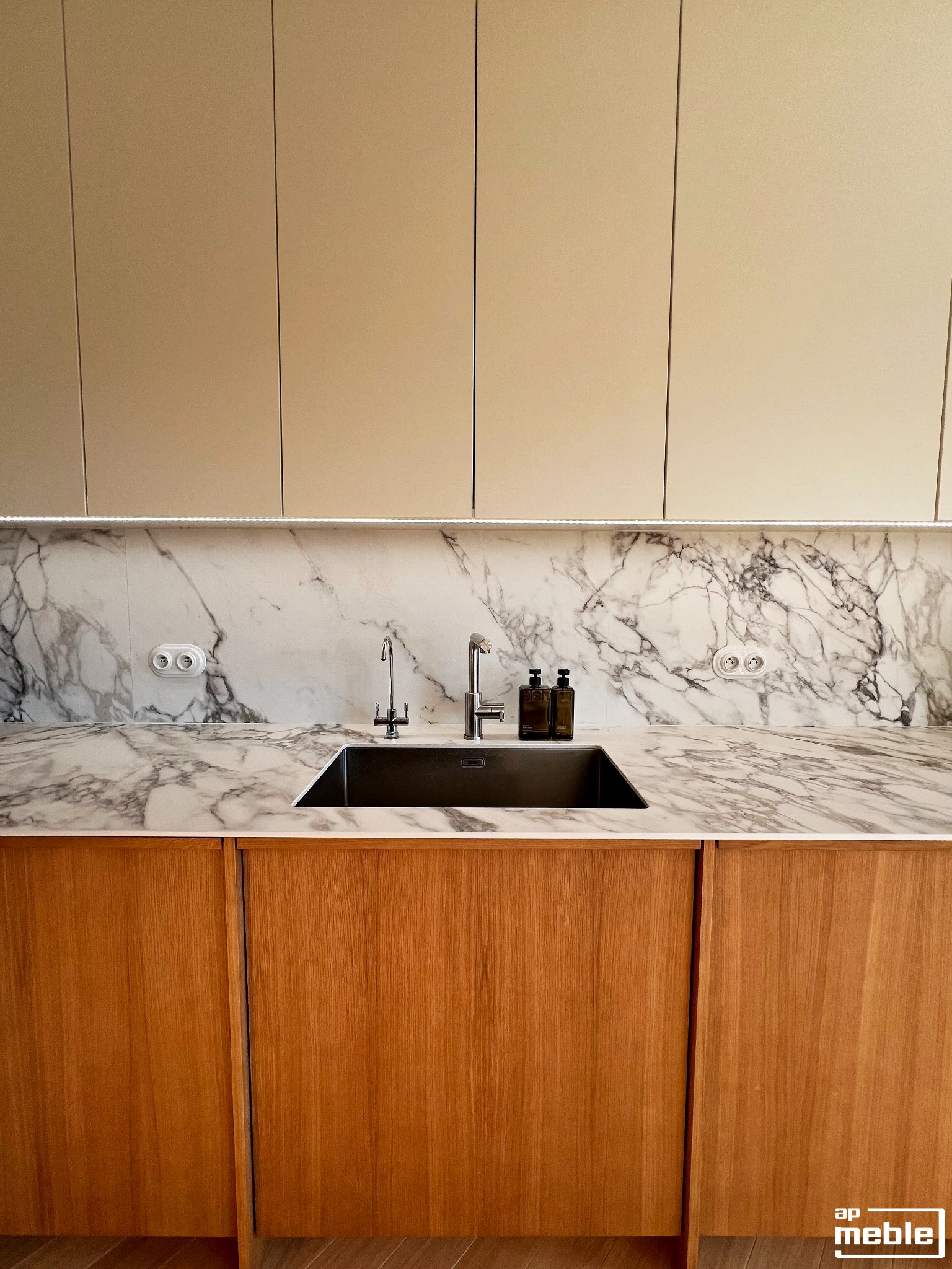 Nowoczesna kuchnia: drewniane szafki dolne, marmurowy blat i ściana, beżowe szafki górne z oświetleniem LED. Minimalistyczny design, armatura kuchenna.