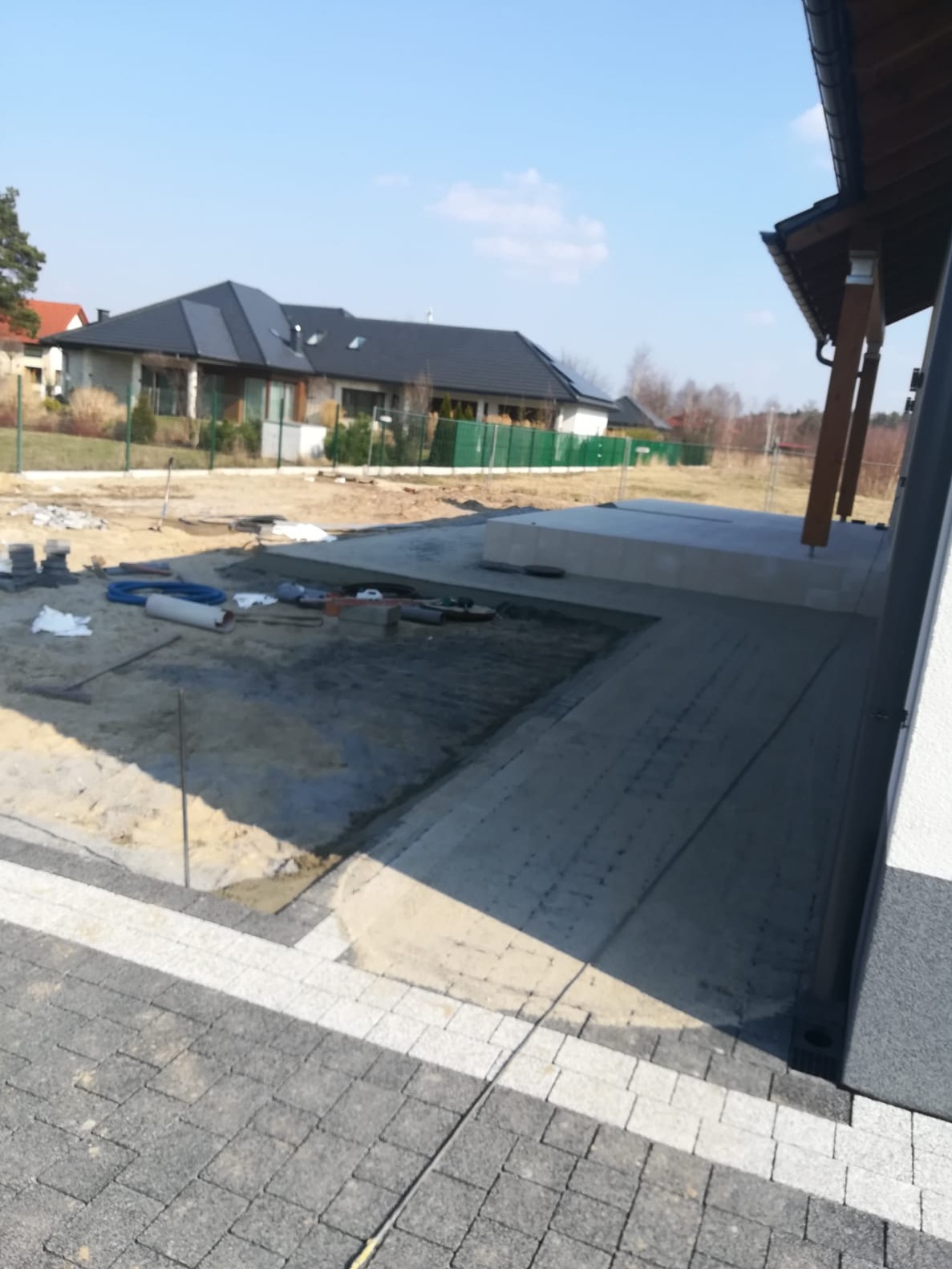 Fragment tarasu w trakcie budowy z widoczną podbudową, częściowo ułożoną kostką i przygotowanym terenem pod dalsze prace, w tle dom jednorodzinny.