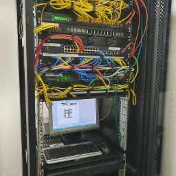 Szafa serwerowa z patch panelem, switchem, okablowaniem Ethernet i monitorem wyświetlającym konfigurację sieci, widoczny rejestrator CCTV IPOX.