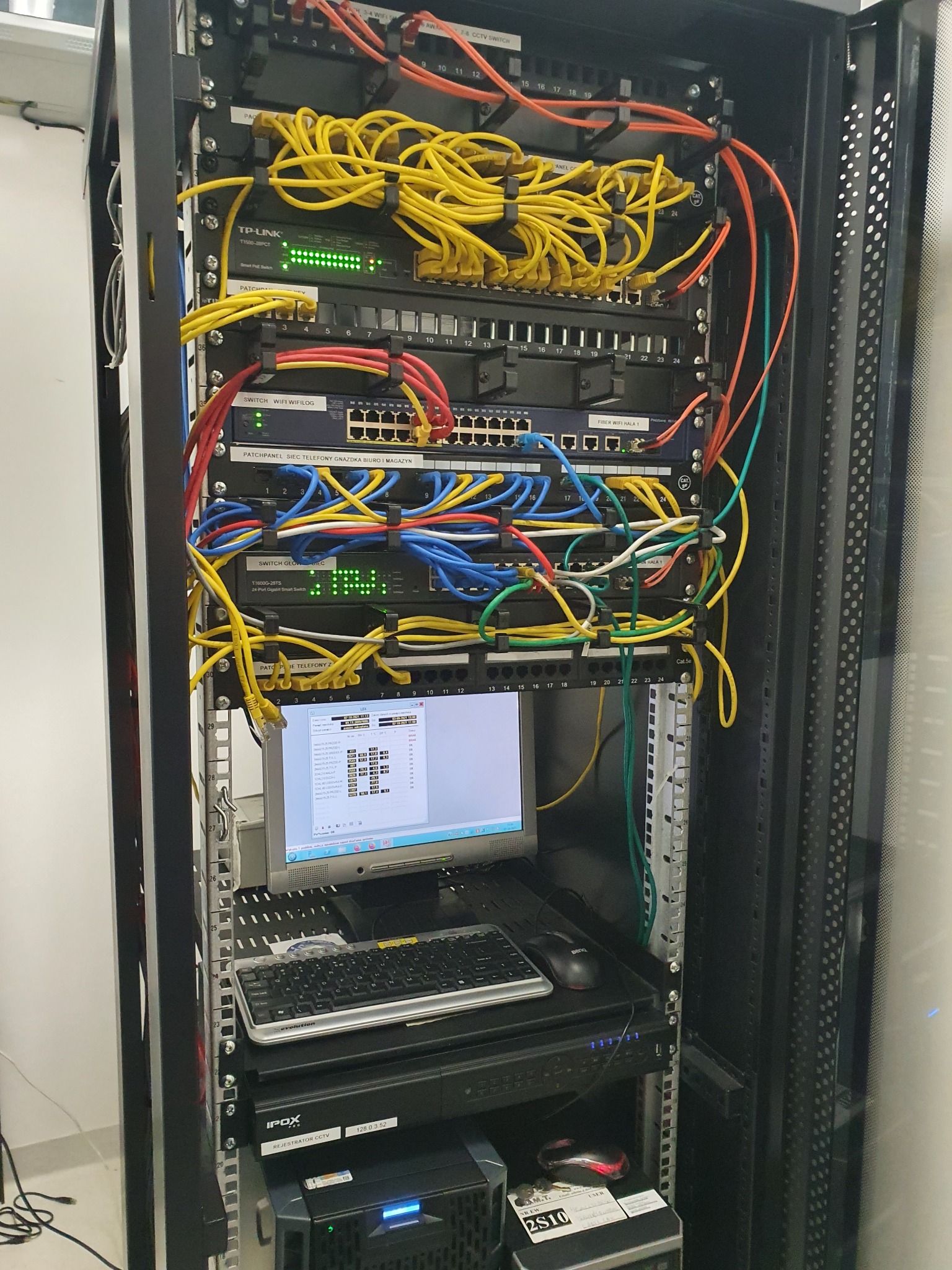 Szafa serwerowa z patch panelem, switchem, okablowaniem Ethernet i monitorem wyświetlającym konfigurację sieci, widoczny rejestrator CCTV IPOX.