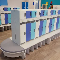 Szatnia z rzędem kolorowych szafek w odcieniach bieli, błękitu i granatu, z drewnianą podłogą i siedziskiem z szarej tapicerki