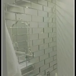 Ściana w łazience wyłożona prostokątnymi lustrami, z widocznym fragmentem wanny i dozownikiem mydła odbitym w lustrach, biała ściana po prawej stronie.