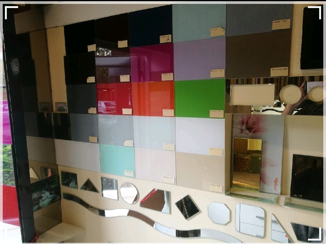 Ekspozycja próbek szkła lacobel w różnych kolorach i kształtach, z widocznymi notatkami z cenami na każdej próbce, prezentowana w showroomie.