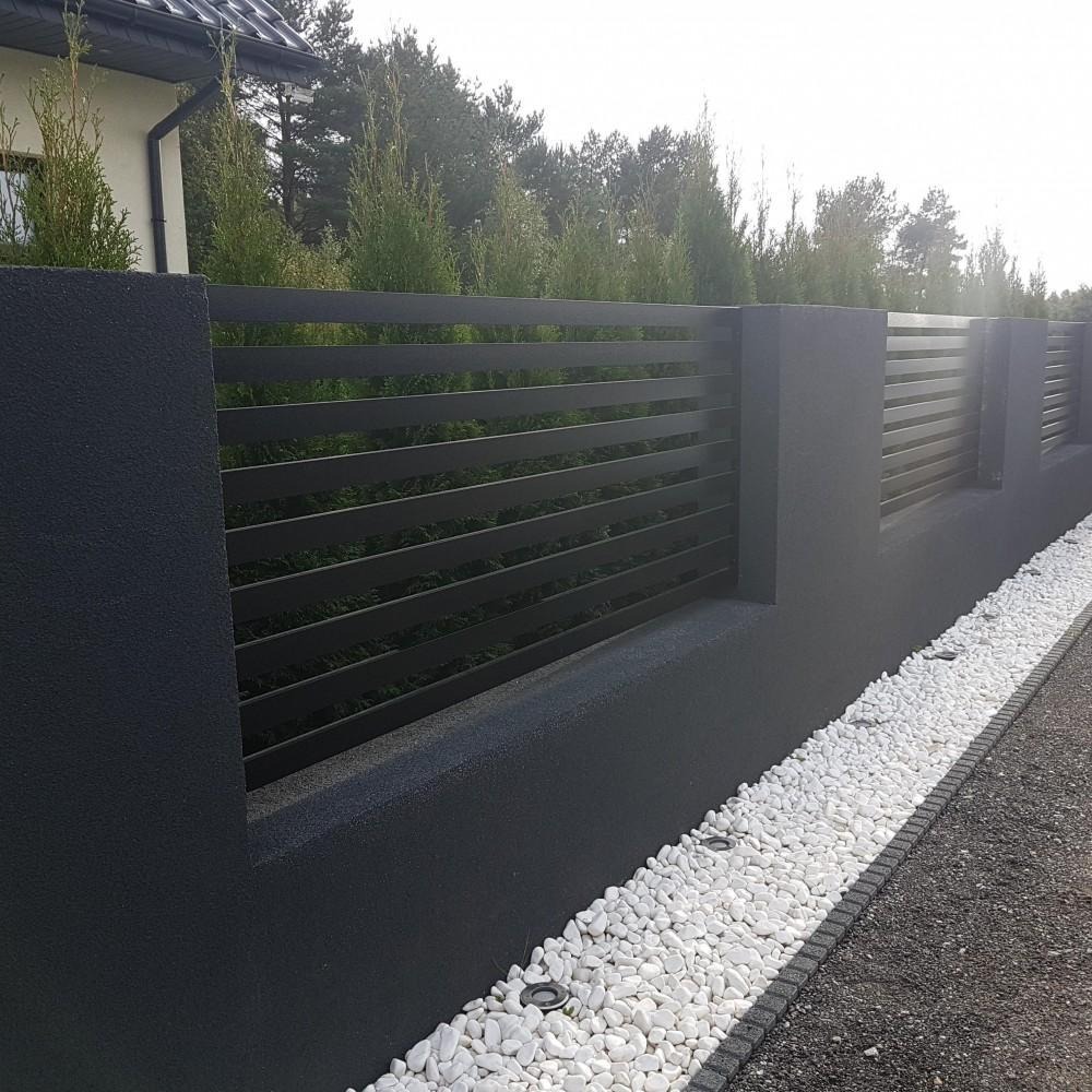 Nowoczesne, poziome, czarne przęsła osadzone w ciemnoszarym, teksturowanym murku z białym kamieniem dekoracyjnym u podstawy, oświetlone punktowymi lampami gruntowymi.