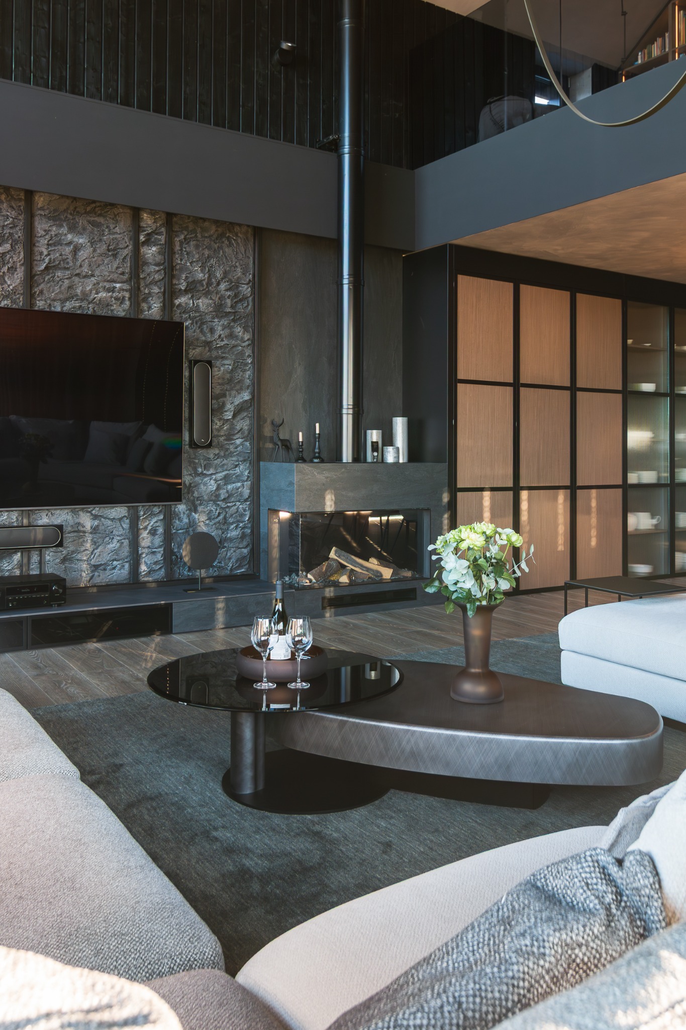 Nowoczesny salon z kamienną ścianą, kominkiem i szklanym stolikiem kawowym z winem. Minimalistyczny design, stonowana kolorystyka, eleganckie dodatki.