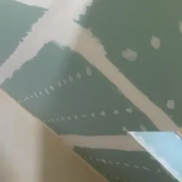 Skośny sufit poddasza z płyt kartonowo-gipsowych, szpachlowane łączenia widoczne na tle zielonej powierzchni płyt.