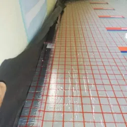 Montaż maty grzewczej w Bolesławcu, widoczne przygotowane podłoże z folią w kratkę i izolacją przy ścianie.