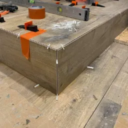 Układanie płytek imitujących drewno na podwyższeniu w łazience, widoczne poziomica, taśma, kliny i krzyżyki dystansowe.