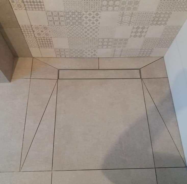 Wykończona podłoga łazienki z odpływem liniowym i wzorzystymi płytkami na suficie, widok z góry.