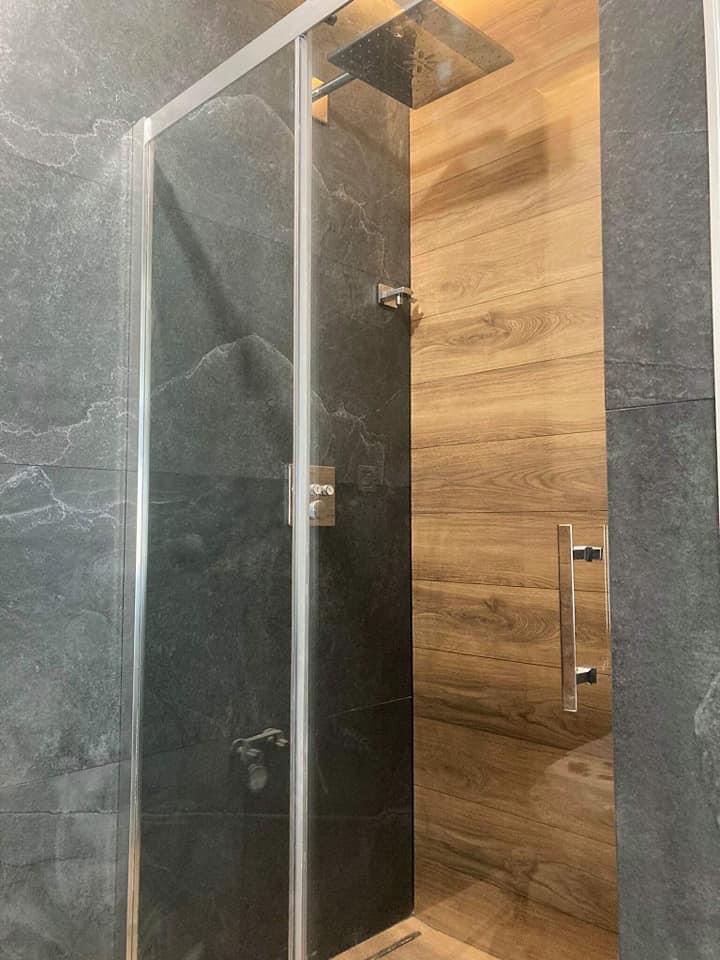 Nowoczesna kabina prysznicowa z szarymi płytkami imitującymi kamień i drewnopodobnymi panelami, z deszczownicą i minimalistyczną armaturą.