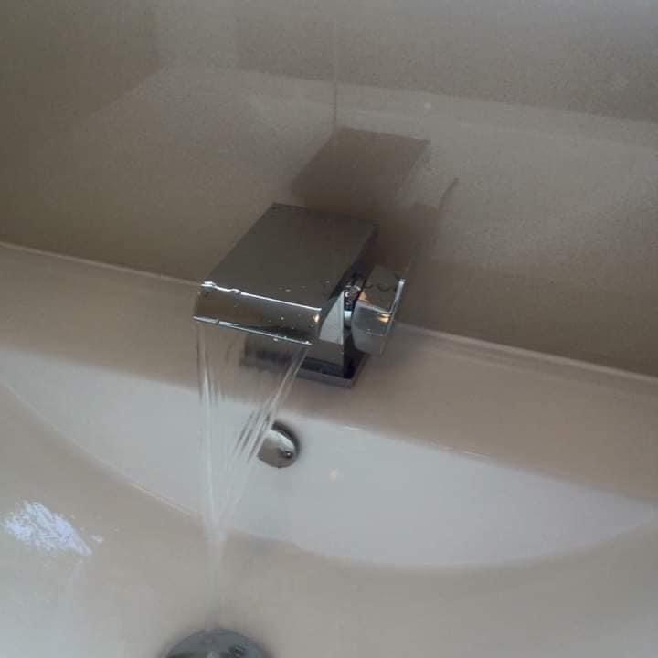 Chromowana bateria umywalkowa z prostokątną wylewką, z której płynie woda, zamontowana w białej umywalce, widok z góry.