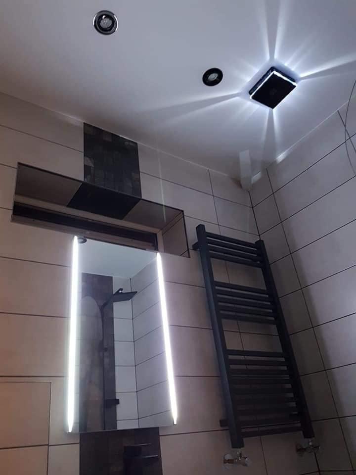 Nowoczesna łazienka z podświetlanym lustrem, grzejnikiem drabinkowym w kolorze antracytowym i punktowym oświetleniem sufitowym.