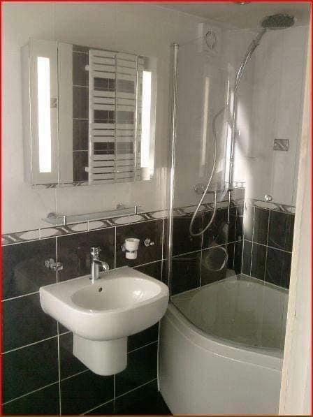 Wykończona łazienka z czarno-białymi płytkami, narożną wanną z prysznicem i podświetlaną szafką z lustrem nad umywalką.