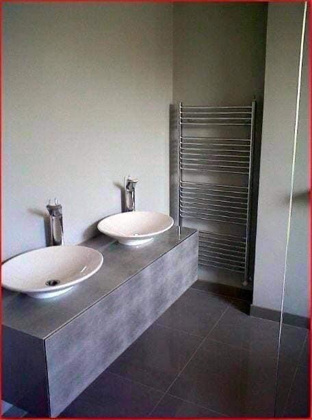 Nowoczesna łazienka z dwoma owalnymi, białymi umywalkami nablatowymi na szarym, betonowym blacie, grzejnik drabinkowy na ścianie, szare płytki podłogowe.