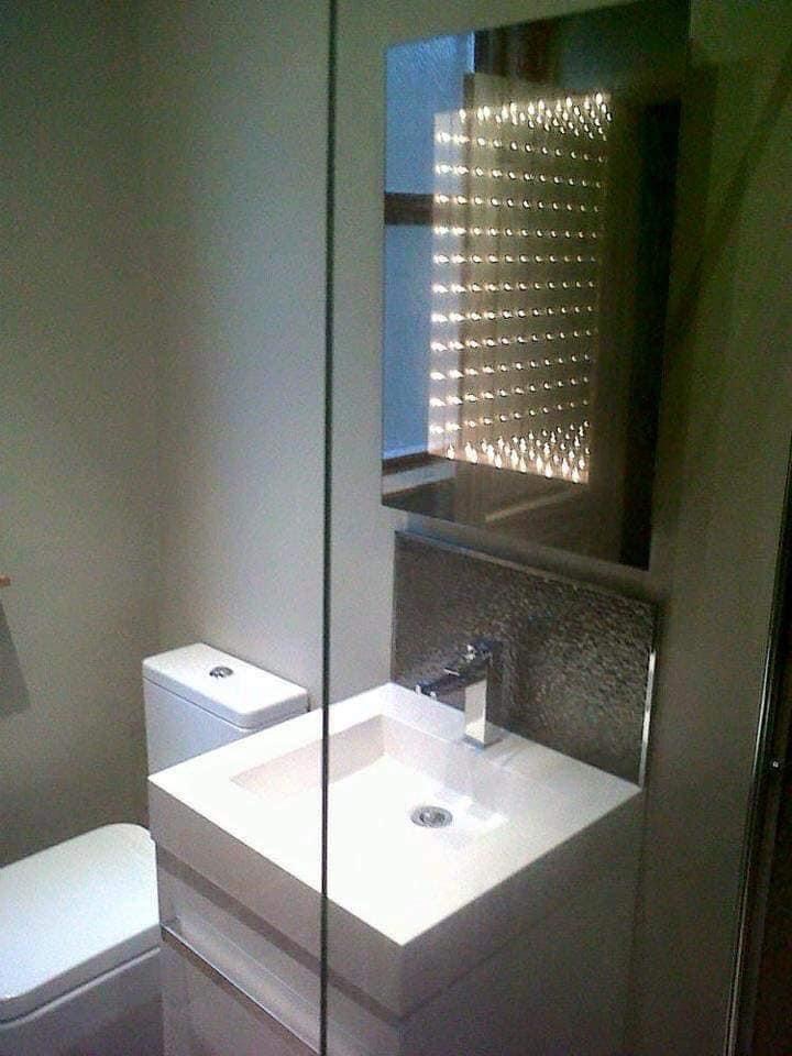 Nowoczesna łazienka z białą, kwadratową umywalką, lustrem z podświetleniem punktowym i szklaną kabiną prysznicową.