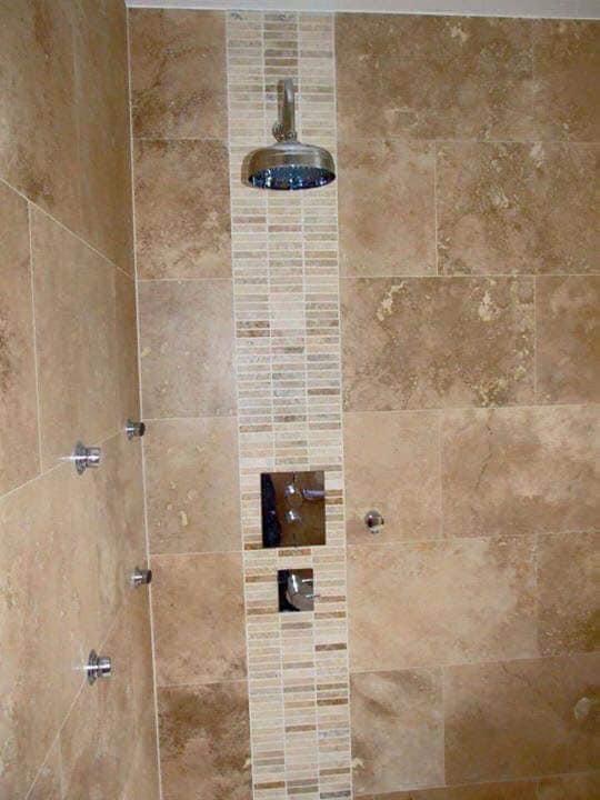 Wykończona kabina prysznicowa z beżowymi płytkami imitującymi kamień, centralny pas z mozaiki w odcieniach beżu, deszczownica i bateria podtynkowa.