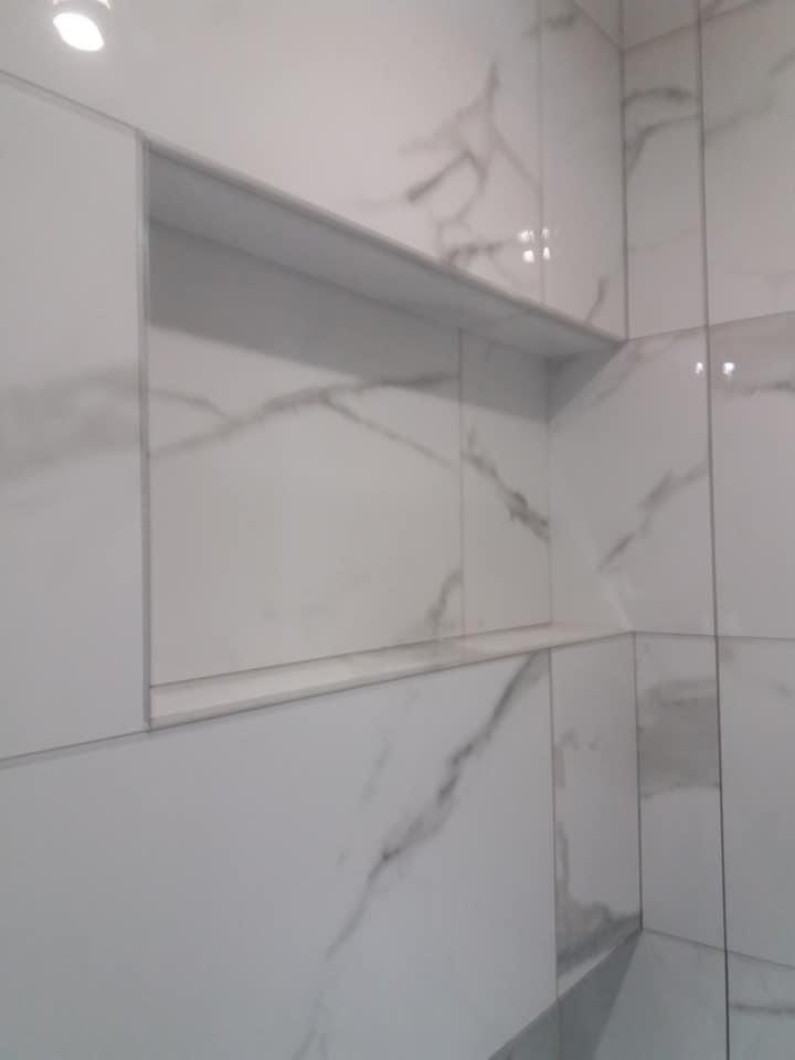 Białe płytki imitujące marmur z wnęką w ścianie wyłożoną tym samym materiałem w łazience, widok na róg ściany