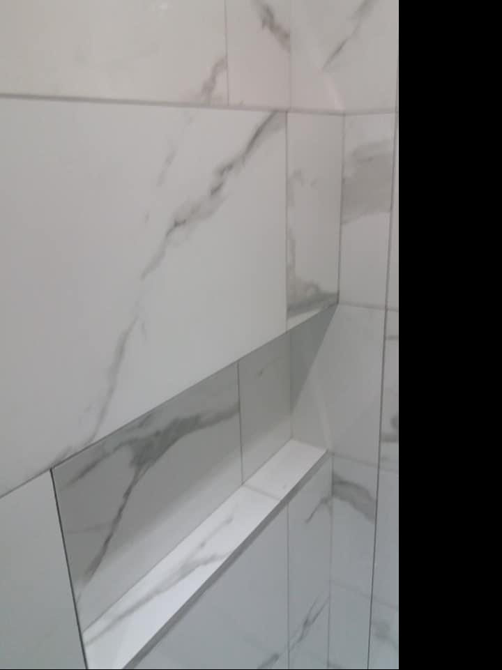 Białe płytki imitujące marmur z wnęką w ścianie, wykończona fuga w kolorze płytek.