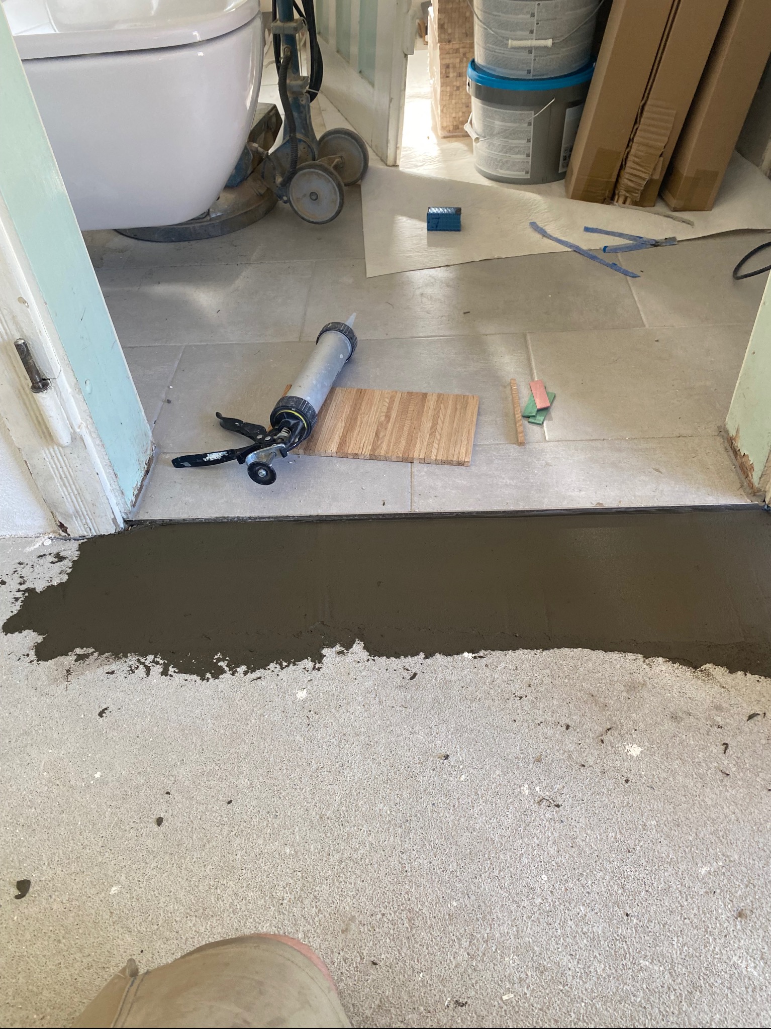 Przygotowanie do położenia podłogi w Lubomierzu: widoczna wylewka wyrównująca, narzędzia (pistolet do silikonu, packa drewniana) i materiały budowlane w tle, sugerujące trwający remont.