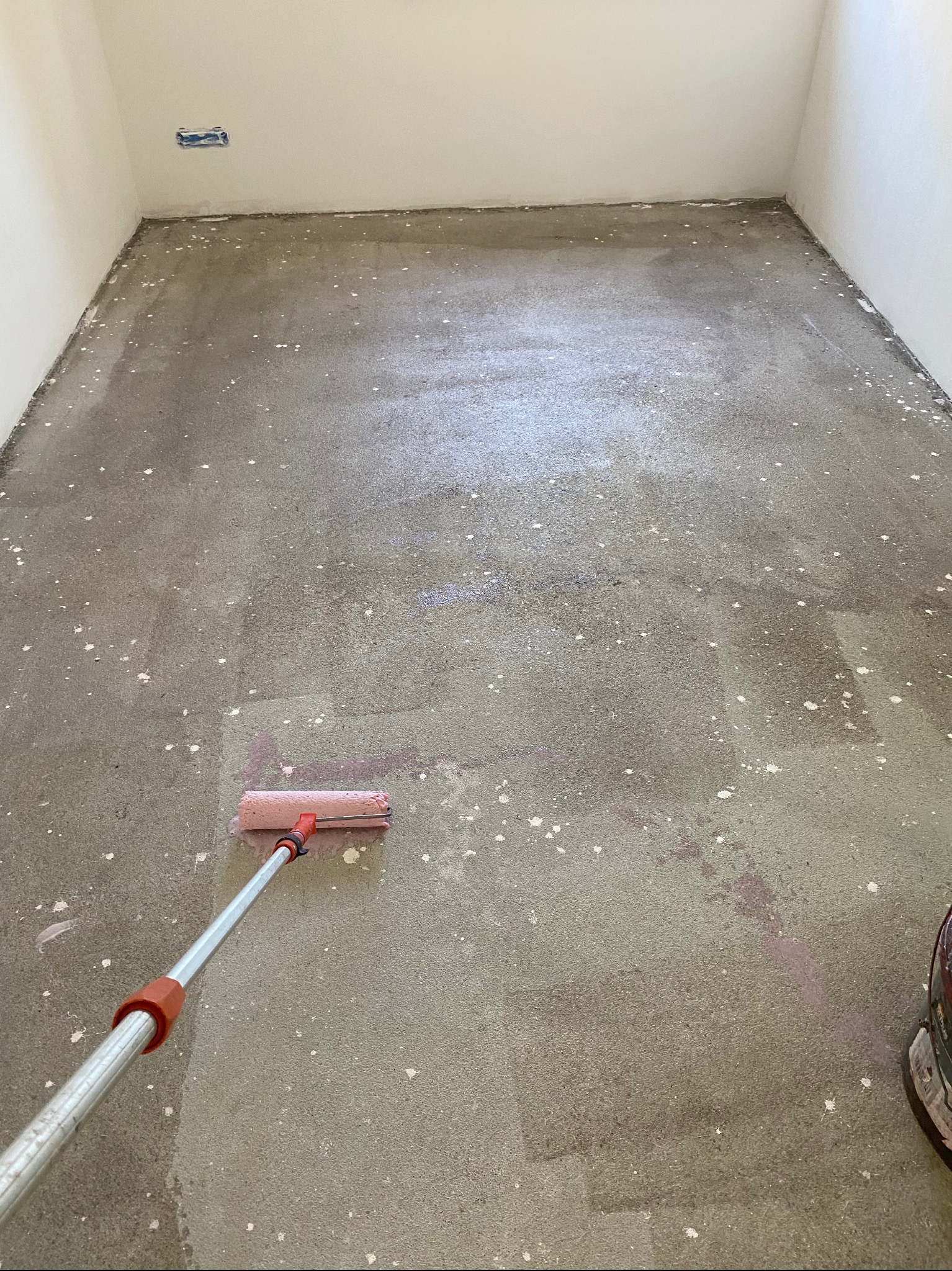 Wyrównywanie wylewki samopoziomującej w pomieszczeniu za pomocą wałka kolczastego, widoczne białe odpryski i ślady różowej farby.