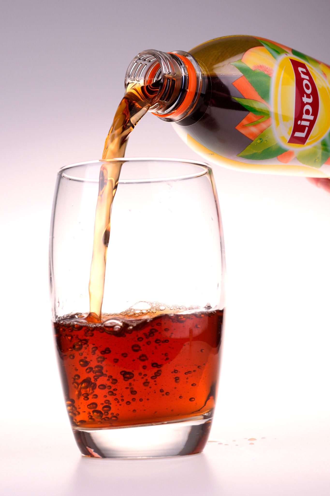 Nalewanie mrożonej herbaty Lipton z butelki do szklanki, widoczne bąbelki w napoju i etykieta butelki z logo.